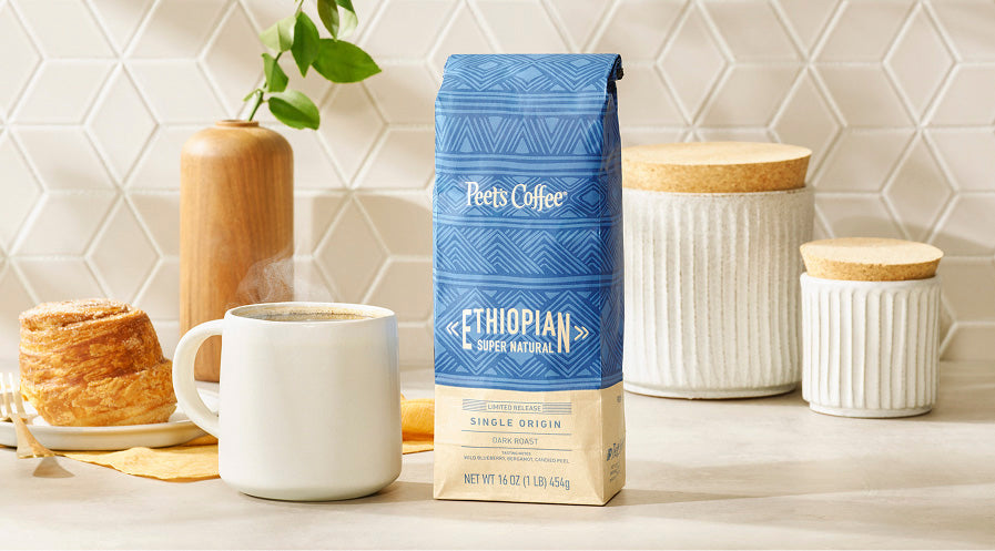 Peet's Coffee Ethiopian Super natural coffee bag with a white mug and pastries on a kitchen counter.